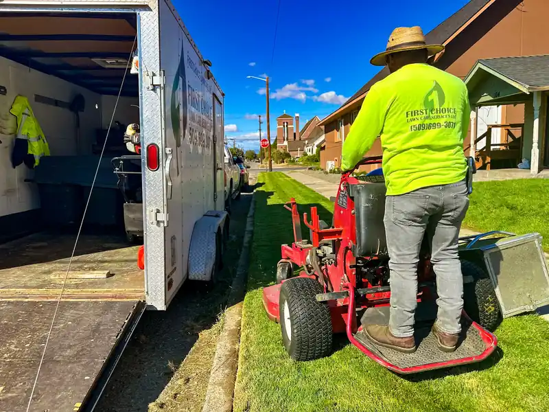 A First Choice crewman in a branded shirt on a stand-on mower beside the company trailer