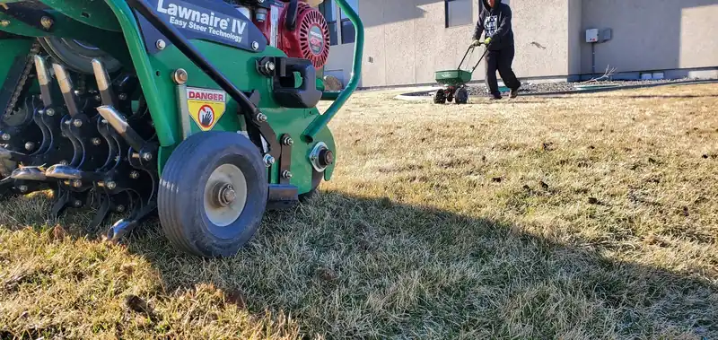 A Lawnaire IV aerator working a dormant lawn with a spreader behind it