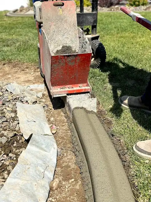 A curbing machine extruding a ribbon of concrete edging along a bed