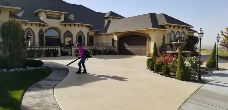 A driveway being blown clean in front of a large stucco home