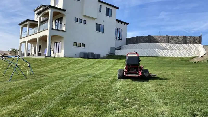 A First Choice riding mower striping a large lawn below a three-storey house